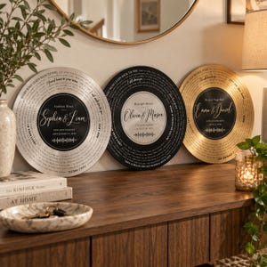 May include: Three circular wall plaques designed like vinyl records, featuring personalized text, names, and dates. The left is silver, the center is black, and the right is gold. Each displays a central label with names and a sound wave graphic.
