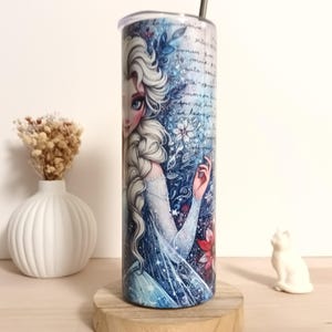 May include: A stainless steel tumbler featuring a detailed illustration of a character with long white hair and a blue dress. The design includes floral and script elements in shades of blue and white. A silver straw is inserted into the lid.