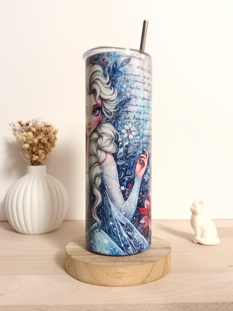 May include: A stainless steel tumbler featuring a detailed illustration of a character with long white hair and a blue dress. The design includes floral and script elements in shades of blue and white. A silver straw is inserted into the lid.