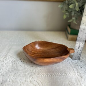 K&ouml;nnte beinhalten: Eine holzfarbene, blattf&ouml;rmige Schale mit Griff. Die Schale besteht aus hellbraunem Holz und hat eine glatte, polierte Oberfl&auml;che. Ein Metalllineal befindet sich neben der Schale. Die Schale ist ca. 18 cm lang.