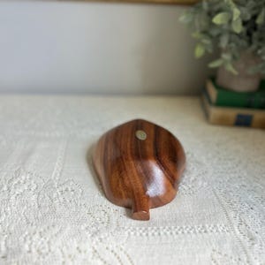 K&ouml;nnte beinhalten: Eine holzfarbene, blattf&ouml;rmige Schale mit dunkelbraunem Finish. Die Schale hat eine glatte, polierte Oberfl&auml;che und einen kleinen, abgerundeten Stiel. Ein kleiner Aufkleber ist auf der Schale sichtbar. Die Schale wird wahrscheinlich zu dekorativen Zwecken verwendet.