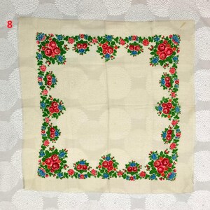 May include: Cream-colored square textile with a floral border. The border features clusters of red roses, blue flowers, and green leaves. The number "8" is visible in the upper left corner.