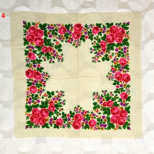 May include: A square, cream-colored scarf with a floral design. The scarf features a border of vibrant pink roses, purple flowers, and green leaves. The floral pattern frames the scarf's center.