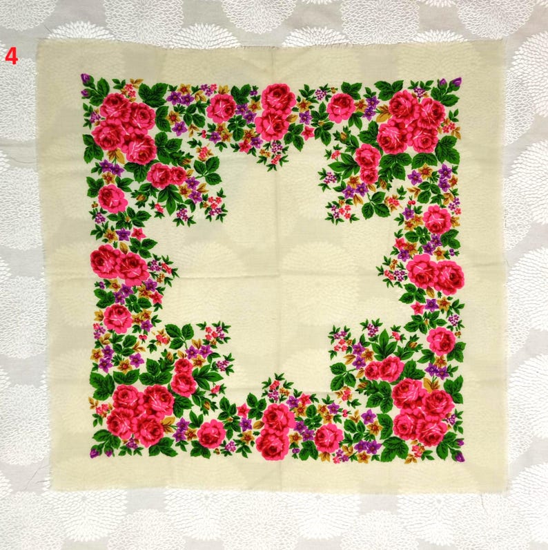 May include: A square, cream-colored scarf with a floral design. The scarf features a border of vibrant pink roses, purple flowers, and green leaves. The floral pattern frames the scarf's center.