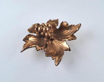 Könnte beinhalten: Eine bronzefarbene, dekorative Blattschale mit einer Traube in der Mitte. Die Schale hat detaillierte Adern und eine strukturierte Oberfläche. Das Design erinnert an einen Weinstock.