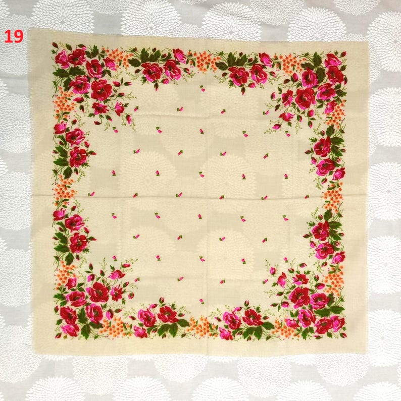 May include: A square, cream-colored scarf with a floral design. The scarf features a border of red roses and green leaves, with smaller pink floral accents scattered across the center. The number "19" is in the upper left corner.