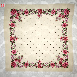 Op de afbeelding: Een vierkante, cr&egrave;mekleurige sjaal met een bloemenrand. De rand heeft grote, roze bloemen en groene bladeren. Kleine zwarte stippen zijn verspreid over de cr&egrave;mekleurige achtergrond. Het nummer "13" staat in de linkerbovenhoek.