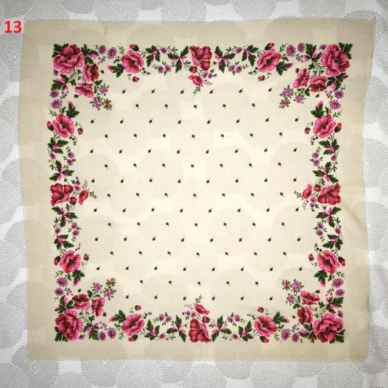 Op de afbeelding: Een vierkante, cr&egrave;mekleurige sjaal met een bloemenrand. De rand heeft grote, roze bloemen en groene bladeren. Kleine zwarte stippen zijn verspreid over de cr&egrave;mekleurige achtergrond. Het nummer "13" staat in de linkerbovenhoek.