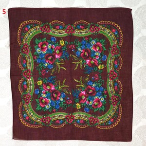 May include: A square, burgundy scarf with a floral design. The scarf features a central pattern of red poppies and blue flowers, framed by a green and yellow border with a scalloped edge. The corners of the scarf are also decorated with floral arrangements.