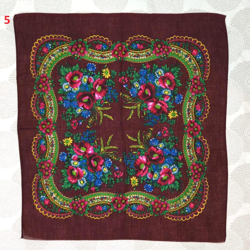 May include: A square, burgundy scarf with a floral design. The scarf features a central pattern of red poppies and blue flowers, framed by a green and yellow border with a scalloped edge. The corners of the scarf are also decorated with floral arrangements.