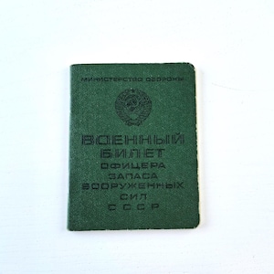 以下が含まれることがあります： 暗い緑色の軍事文書。キリル文字と金のエンブレムが特徴です。長方形で、軍のIDまたは同様の公式記録のようです。テキストは黒色で、白い背景にあります。