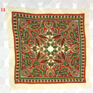 May include: Square scarf with a cream-colored border and a vibrant paisley pattern in red, green, and gold. The scarf features a detailed design with a fringed edge, showcasing a traditional textile pattern.