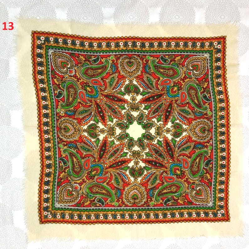 May include: Square scarf with a cream-colored border and a vibrant paisley pattern in red, green, and gold. The scarf features a detailed design with a fringed edge, showcasing a traditional textile pattern.