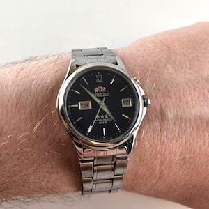 Può includere: Orologio da polso Orient color argento con quadrante nero. L'orologio presenta un display della data e del giorno, e lancette luminose. Ha un cinturino in acciaio inossidabile e un quadrante rotondo. L'orologio è resistente all'acqua fino a 50m.