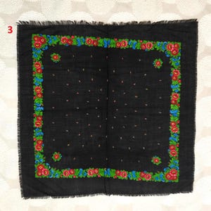 May include: A black square scarf with a floral border. The border features red, blue, and green flowers. The scarf has a fringed edge and small pink dots scattered across the surface.