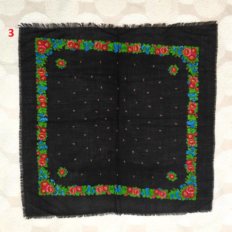 May include: A black square scarf with a floral border. The border features red, blue, and green flowers. The scarf has a fringed edge and small pink dots scattered across the surface.