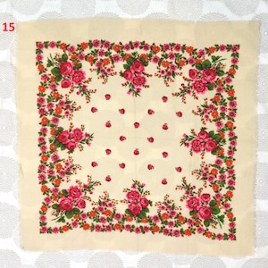 Op de afbeelding: Een cr&egrave;mekleurige vierkante sjaal met een bloemenmotief. De sjaal heeft een rand van rode en oranje bloemen met groene bladeren, rondom clusters van roze rozen. Kleine rode bloemen zijn verspreid over de cr&egrave;mekleurige achtergrond.