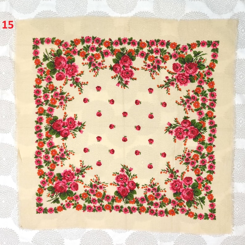 Op de afbeelding: Een cr&egrave;mekleurige vierkante sjaal met een bloemenmotief. De sjaal heeft een rand van rode en oranje bloemen met groene bladeren, rondom clusters van roze rozen. Kleine rode bloemen zijn verspreid over de cr&egrave;mekleurige achtergrond.