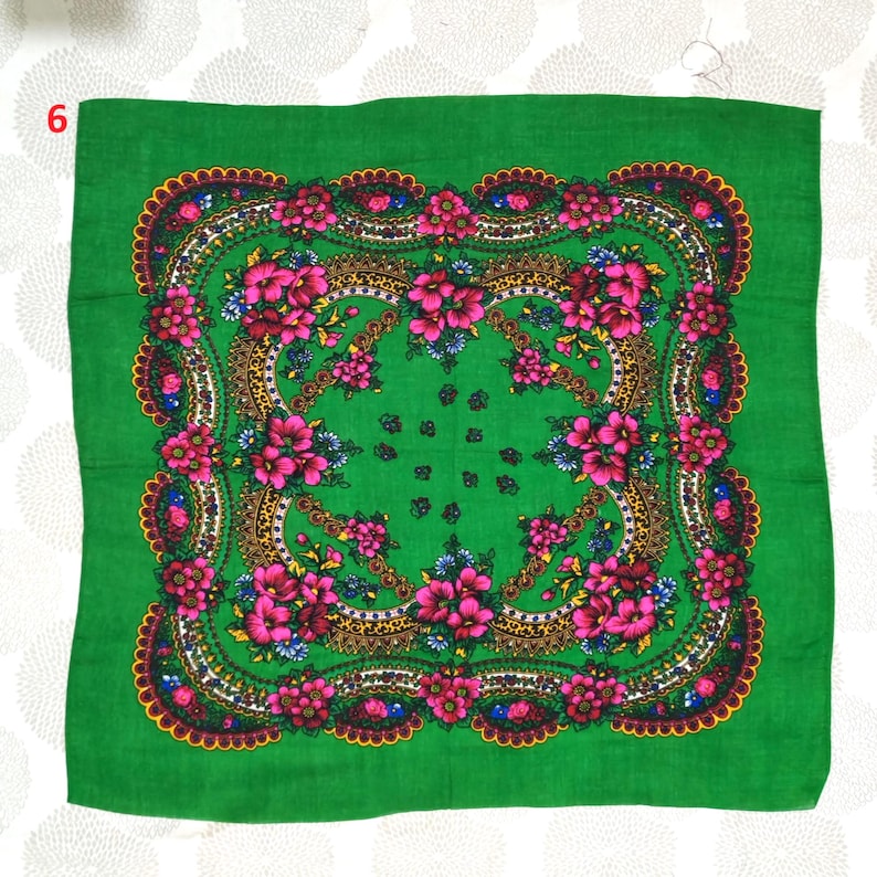 May include: A square, green scarf with a floral design. The scarf features a central pattern of pink flowers, surrounded by a gold and brown border, and a scalloped edge. The background is a solid, bright green.