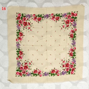 May include: A square, cream-colored scarf with a floral design. The border features red roses, green leaves, and purple berries. The scarf has a fringed edge and small red accents scattered across the center.
