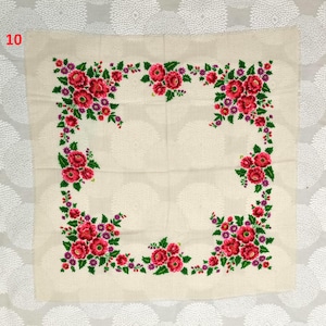 May include: Cream-colored square textile with a floral design. The border features a vibrant arrangement of red flowers, green leaves, and purple accents. The number "10" is in the upper left corner.
