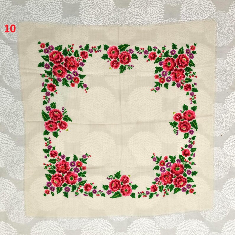 May include: Cream-colored square textile with a floral design. The border features a vibrant arrangement of red flowers, green leaves, and purple accents. The number "10" is in the upper left corner.