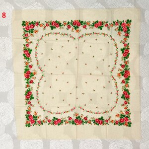 Op de afbeelding: Cr&egrave;mekleurig vierkant textiel met een bloemenontwerp. De rand heeft een guirlande van rode rozen, groene bladeren en oranje accenten. Het midden heeft een subtiel patroon van kleine bloemmotieven.