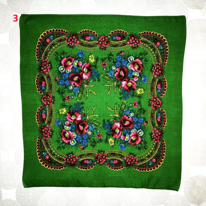Op de afbeelding: Een vierkante, groene sjaal met een bloemenpatroon. De sjaal heeft een centraal patroon van rode en blauwe bloemen, omgeven door een decoratieve rand met rode en gele accenten. De sjaal is gemaakt van zachte stof.