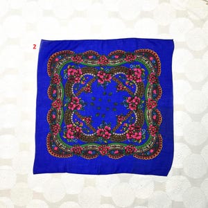 Op de afbeelding: Een vierkante, blauwe sjaal met een bloemenpatroon. Het ontwerp toont roze bloemen en groene bladeren in een bruine rand, tegen een blauwe achtergrond. De sjaal heeft een geschulpte rand.