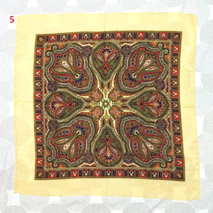 Op de afbeelding: Een vierkante sjaal met een cr&egrave;mekleurige rand en een gedetailleerd paisley patroon. Het centrale ontwerp bevat rode, groene, oranje en blauwe elementen. Het sierlijke ontwerp van de sjaal is geschikt voor mode of decoratie.