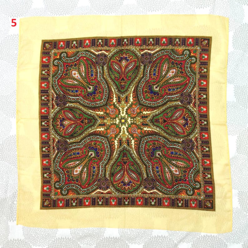 Op de afbeelding: Een vierkante sjaal met een cr&egrave;mekleurige rand en een gedetailleerd paisley patroon. Het centrale ontwerp bevat rode, groene, oranje en blauwe elementen. Het sierlijke ontwerp van de sjaal is geschikt voor mode of decoratie.