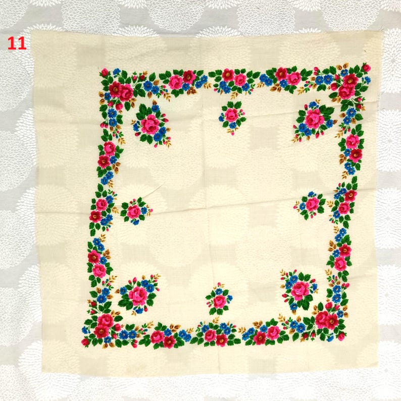 Op de afbeelding: Cr&egrave;mekleurig vierkant textiel met een bloemenrand. De rand heeft roze en rode rozen, blauwe bloemen en groene bladeren. Het nummer "11" staat in de linkerbovenhoek.