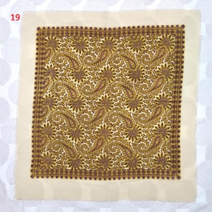 Op de afbeelding: Een vierkante stof met een cr&egrave;mekleurige rand en een gedetailleerd paisley patroon in goud, bruin en paars. Het paisley ontwerp wordt herhaald over het oppervlak van de stof, waardoor een visueel rijk textiel ontstaat. Het nummer "19" staat in de linkerbovenhoek.