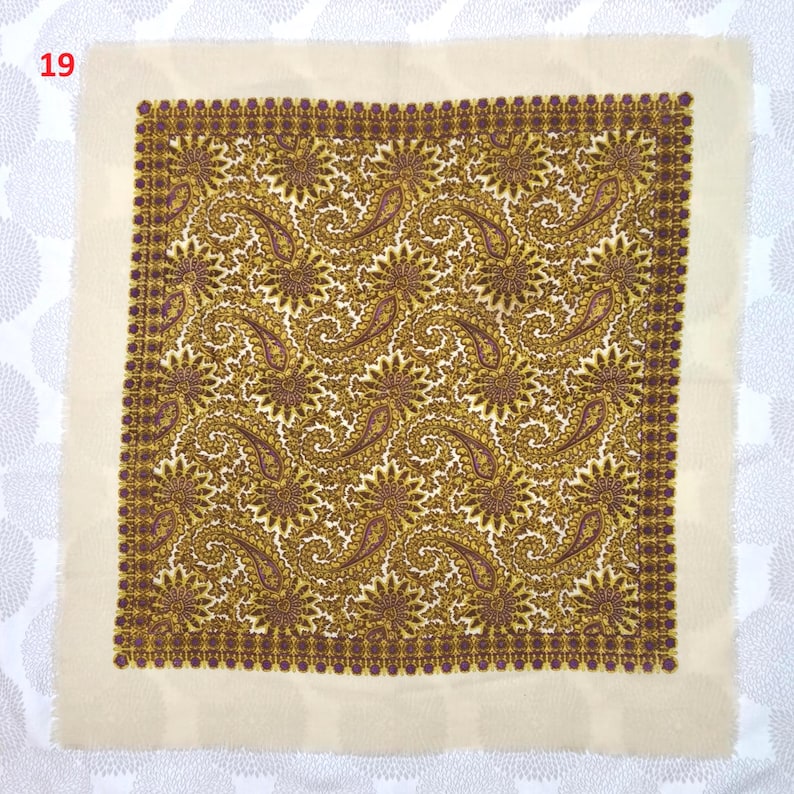 Op de afbeelding: Een vierkante stof met een cr&egrave;mekleurige rand en een gedetailleerd paisley patroon in goud, bruin en paars. Het paisley ontwerp wordt herhaald over het oppervlak van de stof, waardoor een visueel rijk textiel ontstaat. Het nummer "19" staat in de linkerbovenhoek.