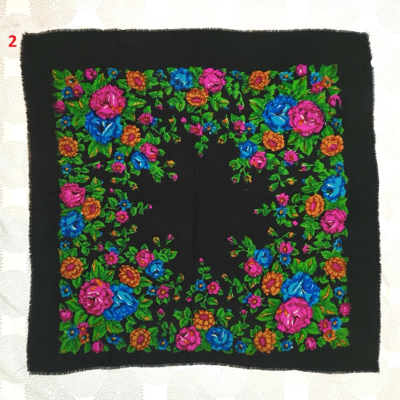 May include: A square black shawl with a vibrant floral pattern. The design features large pink, blue, and orange flowers with green leaves, arranged against a black background. The edges of the shawl have a fringed trim.