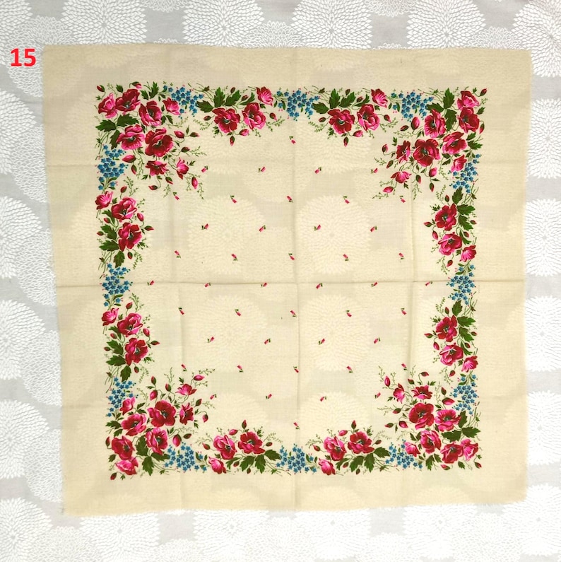 May include: Cream-colored square textile with a floral border. The border features red roses, blue accents, and green leaves. The center has a subtle dotted pattern. The number "15" is in the upper left corner.
