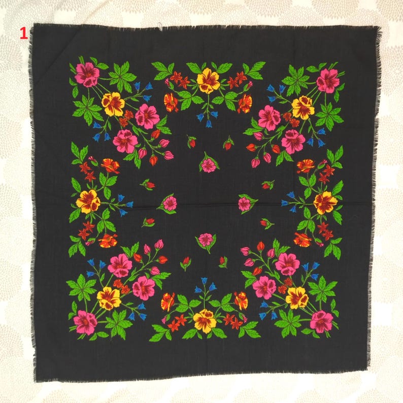 May include: A square black scarf with a floral pattern. The design features pink, yellow, and red flowers with green leaves and blue accents. The scarf has a fringed edge.