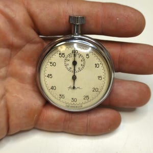 May include: A vintage silver-tone mechanical stopwatch with a round chrome case and a cream-colored dial. The face features black numerals, a smaller sub-dial for minutes, and the Cyrillic text "СДЕЛАНО В СССР" at the bottom edge.
