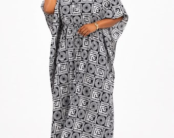Può includere: Un abito caftano lungo fino ai piedi con un motivo geometrico bianco e nero composto da cerchi e quadrati ripetuti. Il capo presenta uno scollo a V, maniche ampie in stile kimono e una vita leggermente segnata, creando una silhouette fluida.