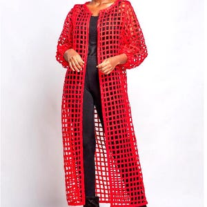 May include: A long, bright red open-front duster cardigan featuring a structured grid-like cutout pattern throughout the fabric. The garment has long sleeves with gathered cuffs and falls to a calf-length hem, worn over a black base layer.