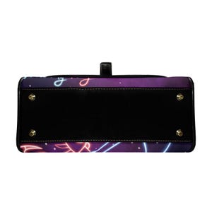 Peut inclure: Un sac &agrave; main noir avec un motif n&eacute;on violet et bleu. Le sac a une poign&eacute;e noire et des pieds dor&eacute;s. Le motif n&eacute;on pr&eacute;sente des lignes et des formes courbes sur un fond violet fonc&eacute;.