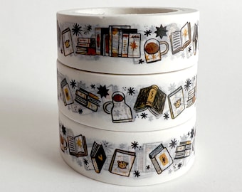 May include: Three rolls of white washi tape stacked on top of each other. Each roll is decorated with a repeating pattern of books, coffee mugs, and stars in shades of brown, black, and yellow. The tape is designed for crafting and scrapbooking.
