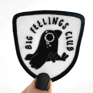 May include: Black and white embroidered patch with a black bird with a teardrop, surrounded by the text "Big Feelings Club".