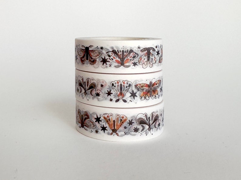 May include: Three rolls of white washi tape with a repeating pattern of black and orange butterflies and stars.