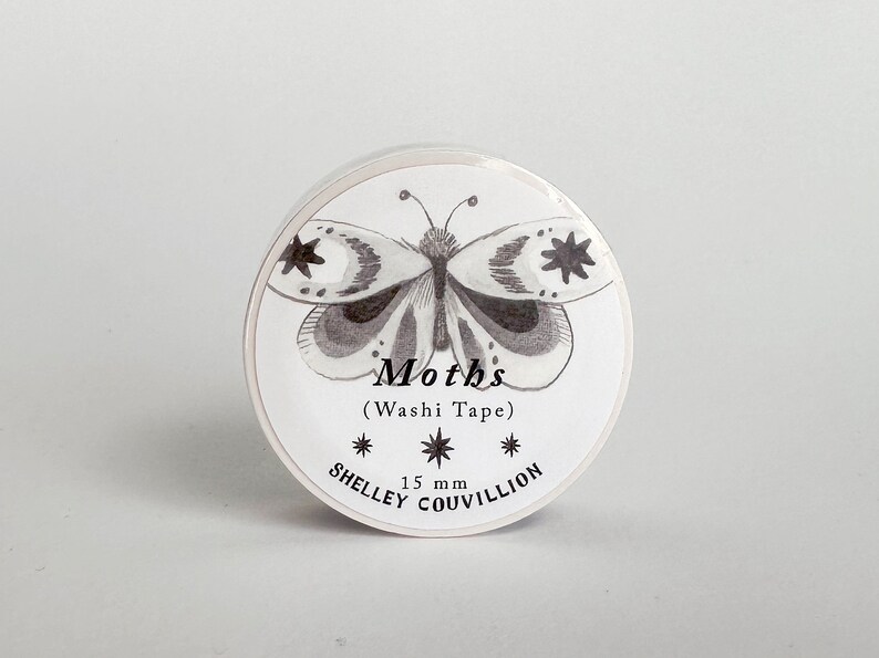 May include: A white roll of washi tape with a black and white illustration of a moth. The text "Moths (Washi Tape)" and "15 mm" are printed on the tape. The text "SHELLEY COUVILLION" is printed on the bottom of the tape.