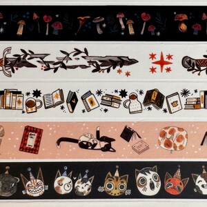 May include: A set of six washi tapes featuring various illustrations, including moths, mushrooms, swords, books, cats, and stars. The tapes are printed on a white background with black and brown accents.