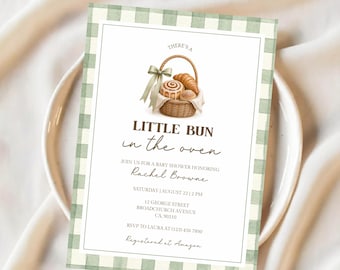 Op de afbeelding: Babyborrel uitnodiging met een groene ruitjesrand. De uitnodiging toont een aquarel illustratie van een mand met gebak en de tekst "LITTLE BUN in the oven". Details: naam, datum, tijd en locatie.