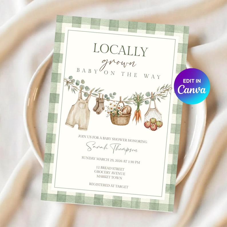 Op de afbeelding: Een uitnodigingskaart voor een babyshower met een groen-witte ruitjesrand. De tekst luidt LOCALLY grown BABY ON THE WAY. Een illustratie toont een waslijn met baby-tuinbroekjes, sokjes, een mand met bloemen, wortels en appels in een nettas.