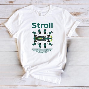 May include: White t-shirt with the word "Stroll" in green block letters above a green and yellow race car graphic. The Aston Martin logo is below the car. The shirt is made of a soft material.