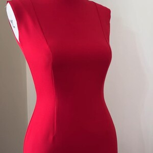 K&ouml;nnte beinhalten: Ein leuchtend rotes, &auml;rmelloses Kleid auf einer Schaufensterpuppe. Das Kleid hat eine figurbetonte Silhouette, einen runden Ausschnitt und eine Naht am R&uuml;cken. Das Kleid ist aus einem glatten, einfarbigen Stoff gefertigt.